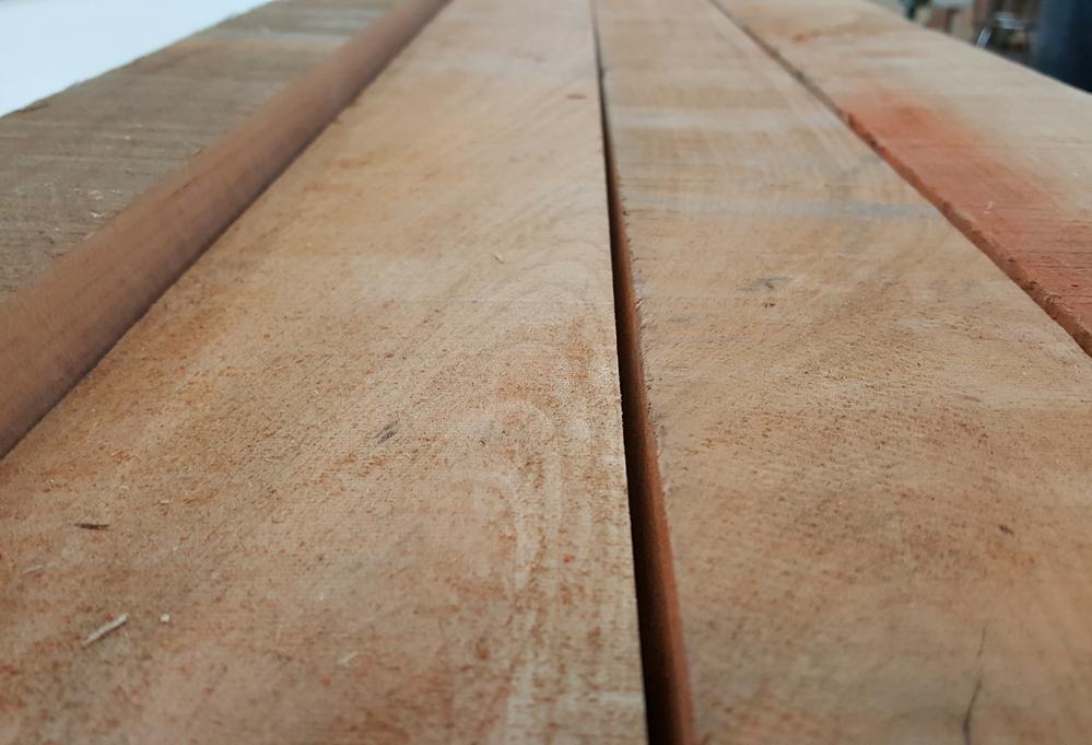 An image of four Rough-Sawn lumber boards laid out on a white colored saw table.