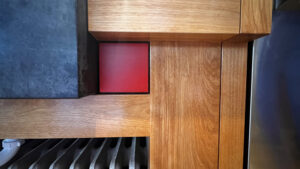 This image also appears in the Cabinet Details Gallery" with the description: This image shows a red painted wood accent square standing out against the side of the blackness of an oiled Soapstone sink, and natural finish of the Birch wood cabinets. This cabinet surrounds a radiator beneath at the bottom of the image. Glen Ellyn Hilltop Gallery