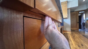 This image shows a hand about to open a slotted drawer pull on the underside of the drawer front. The top drawer of this kitchen cabinet extends 2" further to allow the finger pull to work.