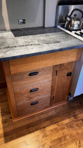 A close up view of the Birch wood base cabinet to the Left of the range on the range wall. In the cabinet to the left of the range there is one top drawer that extends the whole width of the cabinet. Beneath that drawer set 2" back on the Left in this cabinet are 3 stacked drawers. In this cabinet on the right is a tray storage compartment that is the height of the tree lower drawers. Glen Ellyn Hilltop Gallery