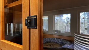 This image shows a close up of the cabinet door oil rubbed bronze latch hardware on this double door Birch wood cabinet to the right of the range hood on the range wall. 