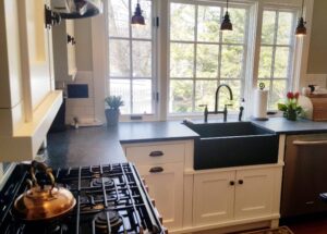 This Image shows the Sink wall elevation with white Poplar painted wood cabinets. It also shows a Soapstone Sink and Soapstone Countertops centered in front of three kitchen windows.