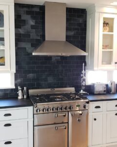 This image shows the AGA Stove and Chimney hood. Soapstone Tile backsplash is installed on the wall behind it.