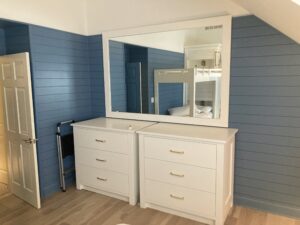 This image shows the two dressers with 3 drawers apiece. The mirror above reflecting the bunks in the background The blue and white walls are behind the dresser and mirror.