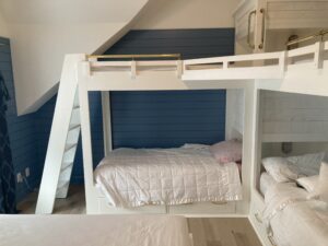 This image shows the two Bunks with four beds standing in front of the dressers facing towards the beds with the blue and white walls behind them. You can also see part of a queen sized bed in the lower left part of the frame.